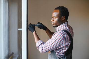 African american Workman in overalls installing or adjusting plastic windows in the living room at...