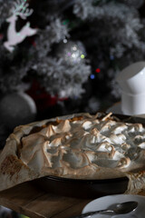 Homemade meringue cake on a wooden table near a decorated New Year tree