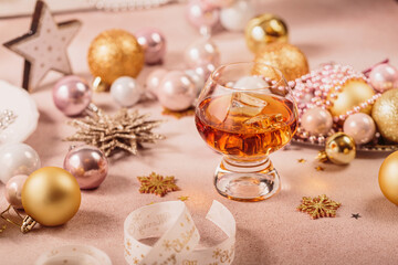 Glass of whiskey or bourbon with festive Christmas decoration on light beige background. New Year, Christmas and winter holidays whiskey mood concept