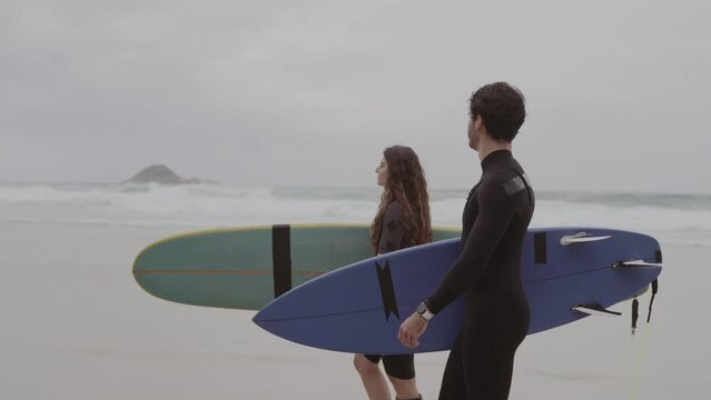 Casal de surfistas caminhando na praia com as pranchas debaixo do braco, conversando. Cinematografico 4k.