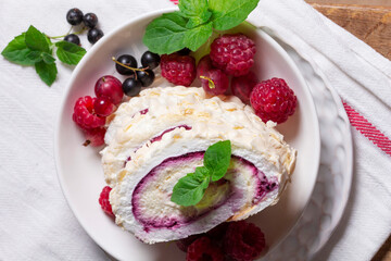 Meringue roll with whipped cream and currant curd, served with berries on a ceramic plate. Rustic style.