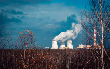 Nuclear power plant cooling towers concept photo. Big chimneys. Forest with partly cloudy sky in Polish province. - obrazy, fototapety, plakaty