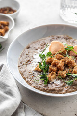 Thick lentil soup with croutons and meat chips served for dinner on white background close up