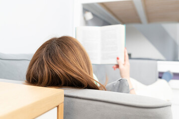Young attractive woman lying on the couch and reading a book. Home education and leisure time...