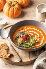 Pumpkin cream soup decorated with cream, pumpkin seeds, bacon, microgreens and olive oil on brown textured background with ingredients