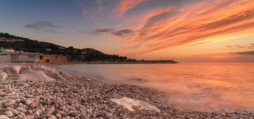 panorama landscape of a colourful sunrise over the white pebble beach and harbor of Mattinata in Italy