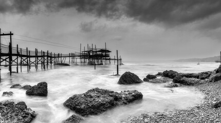 black-and-white view of the Trabocco Cungarelle pile dwelling on an overcast an rainy day on the...