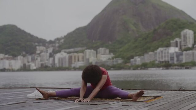 Mulher de meia idade se alongando, praticando ioga, sentada em um pier a beira mar. Cinematico 4k.