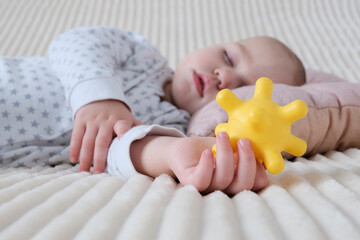 A baby is sleeping in a crib, a child of European appearance, wearing a light light jumpsuit. A yellow rubber toy in the hand. Sleep patterns for babies, care and hygiene.