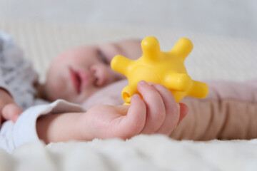 A baby is sleeping in a crib, a child of European appearance, wearing a light light jumpsuit. A yellow rubber toy in the hand. Sleep patterns for babies, care and hygiene.
