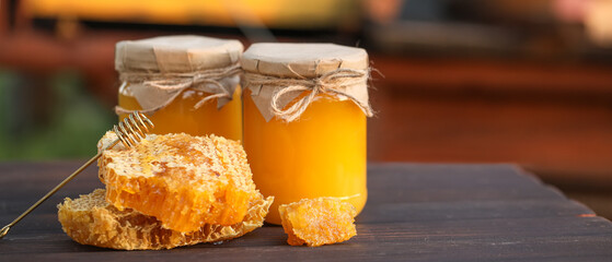 Jars of sweet honey and combs on table at apiary