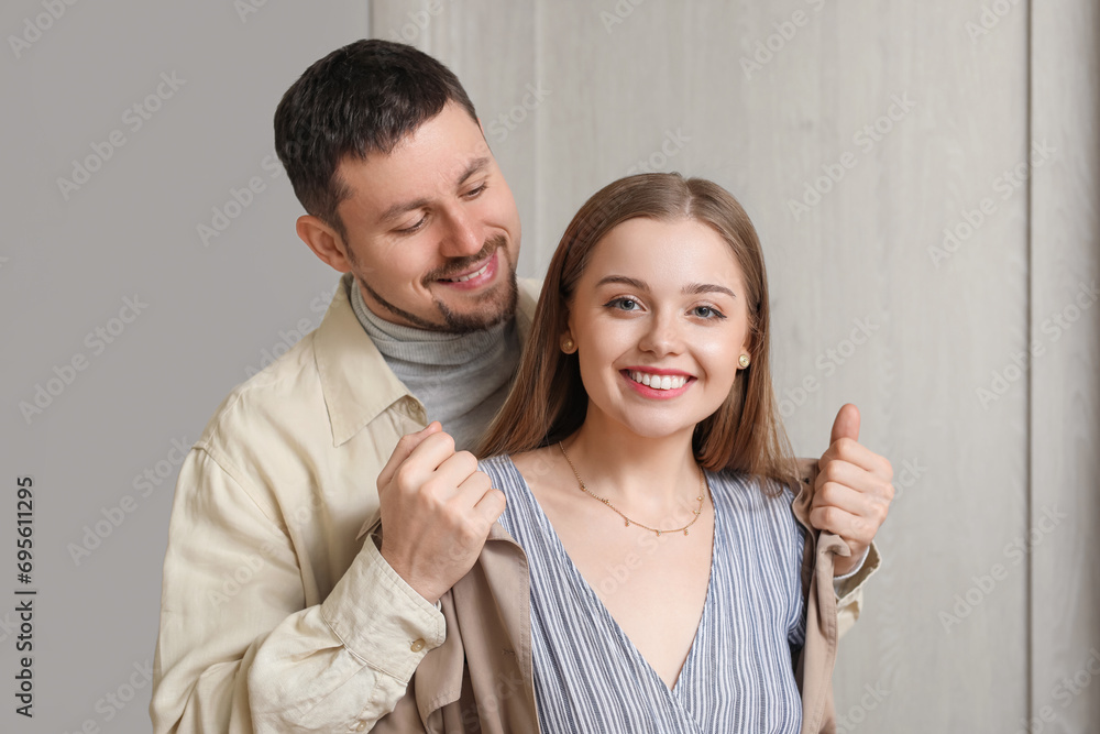 Poster young man putting coat on his wife at home