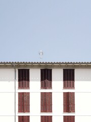 Traditional white Mediterranean-style house with wooden shutters, surrounded by greenery under a clear sky.