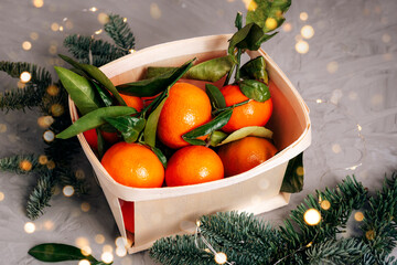 Tangerines in a basket with christmas lights on gray background. Top view