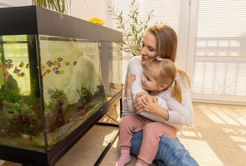 Little girl watching fishes in fish tank with her mother