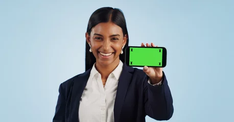 Tuinposter Happy business woman, phone and green screen for advertising against a blue studio background. Portrait of female person or employee smile showing mobile smartphone display, chromakey or mockup space © Wesley JvR/peopleimages.com