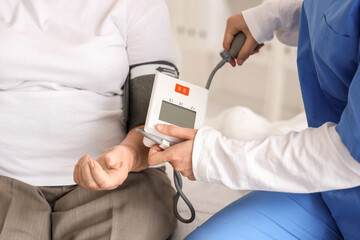 Female nurse measuring blood pressure of senior woman in bedroom, closeup