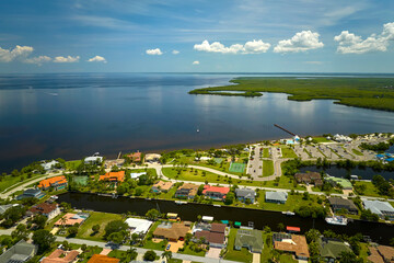 Aerial view of residential suburbs with one storey houses located near wildlife wetlands with green tropical vegetation on sea shore. Living close to nature in warm climate concept - obrazy, fototapety, plakaty