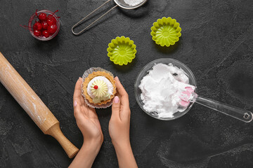 Female confectioner with tasty cake and ingredients on black background