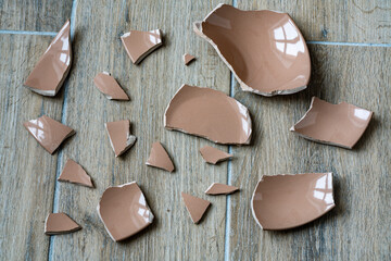 Broken ceramic beige plate on floor in kitchen, closeup. Shards and pieces of a broken dish