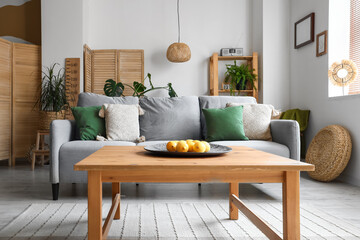 Cozy grey sofa and plate with lemons on wooden coffee table in interior of living room