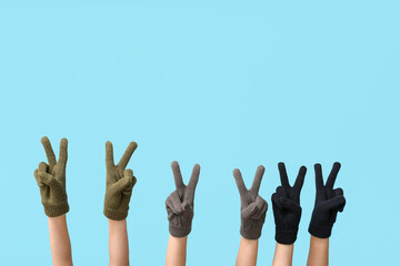 Hands in warm gloves showing victory gestures on blue background