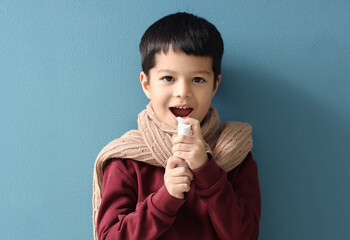 Ill little Asian boy using spray for sore throat on blue background