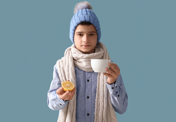 Sick little boy in hat with cup of tea and lemon on blue background