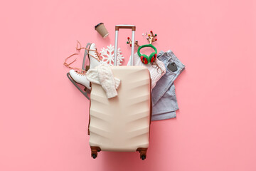 Suitcase with warm clothes, ice skates, Christmas deer horns and cup of coffee on pink background....