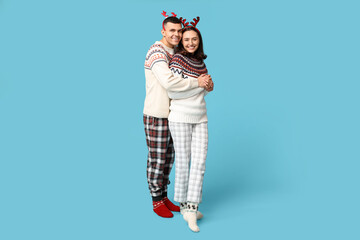 Fototapeta premium Happy young couple in Christmas pajamas hugging on blue background
