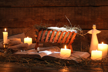 Angel, burning candles and manger with dummy of baby on brown wooden background. Concept of Christmas story - obrazy, fototapety, plakaty