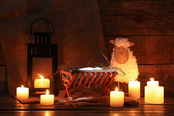 Toy sheep, burning candles and manger with dummy of baby on brown wooden background. Concept of...