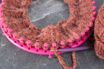 Soft, wool, yarn in a burnt orange color.  Pink loom knitting ring with both knit and pearl stitches.