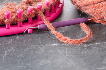 Soft, wool, yarn in a burnt orange color.  Pink, round knitting loom with hook tool and yarn.