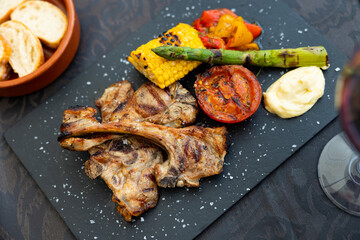 Appetizing grilled juicy mutton chops with vegetable garnish of baked bell peppers, asparagus, tomato and slice of corn on cob served with mayonnaise on slate board