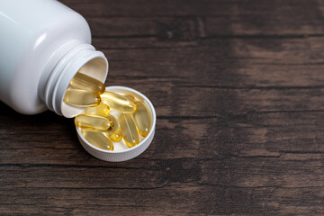 Closeup of omega 3 capsules lie in white bottle on a wooden table. Fish oil tablets top view....