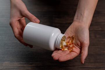 Woman doctor nutritionist hands holds omega 3, vitamin D capsules on a wooden table.