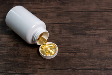 Closeup of omega 3 capsules lie in white bottle on a wooden table. Fish oil tablets top view....