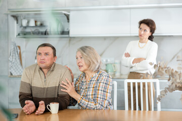 Aggrieved middle-aged man sitting at the kitchen-table after brawling with wife and old woman...