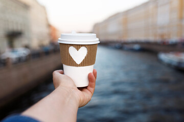 paper cup of natural coffee in woman's palm on background of Moika river in St. Petersburg in...