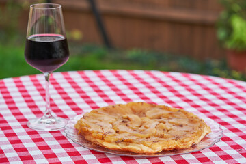 Tarte tatin served with glass of red wine outside in the graden of small restaurant or bistro. Traditional simple apple dessert from French cuisine made from puff pastry, butter and caramelized apples