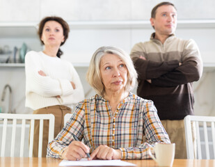 Obraz premium Competitive middle-aged man and woman conflicting and old woman writing inheritance sitting at kitchen table