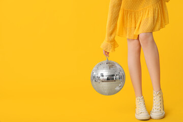 Beautiful young trendy woman with disco ball on yellow background