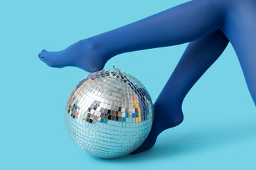 Female legs in stylish tights with disco ball on blue background