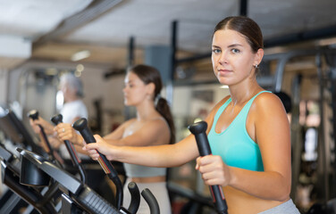 Slender athletic girl during cardio exercises on elliptical simulator in fitness center. Sports to...