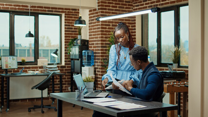Fototapeta na wymiar African american people planning report with annual data on papers and laptop, using online statistics to plan business development. Man and woman reviewing startup results in boardroom.