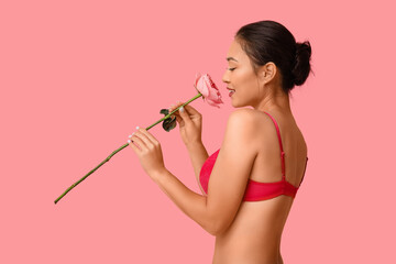 Beautiful young happy Asian woman in sexy underwear with rose on pink background. Valentine's Day...