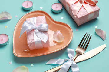 Beautiful table setting for Valentine's Day with pink rose petals, candles and gift boxes on turquoise background