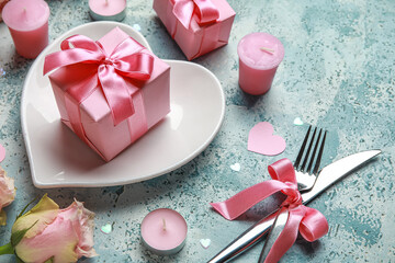 Beautiful table setting for Valentine's Day with pink roses, candles and gifts on blue grunge...