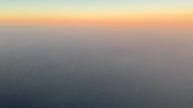 Aerial view of offshore wind farm with wind turbines on the North Sea, the Netherlands, Europe. Several large white and yellow wind turbines, wind mills on a blue, calm, sea. High quality Stock 4K